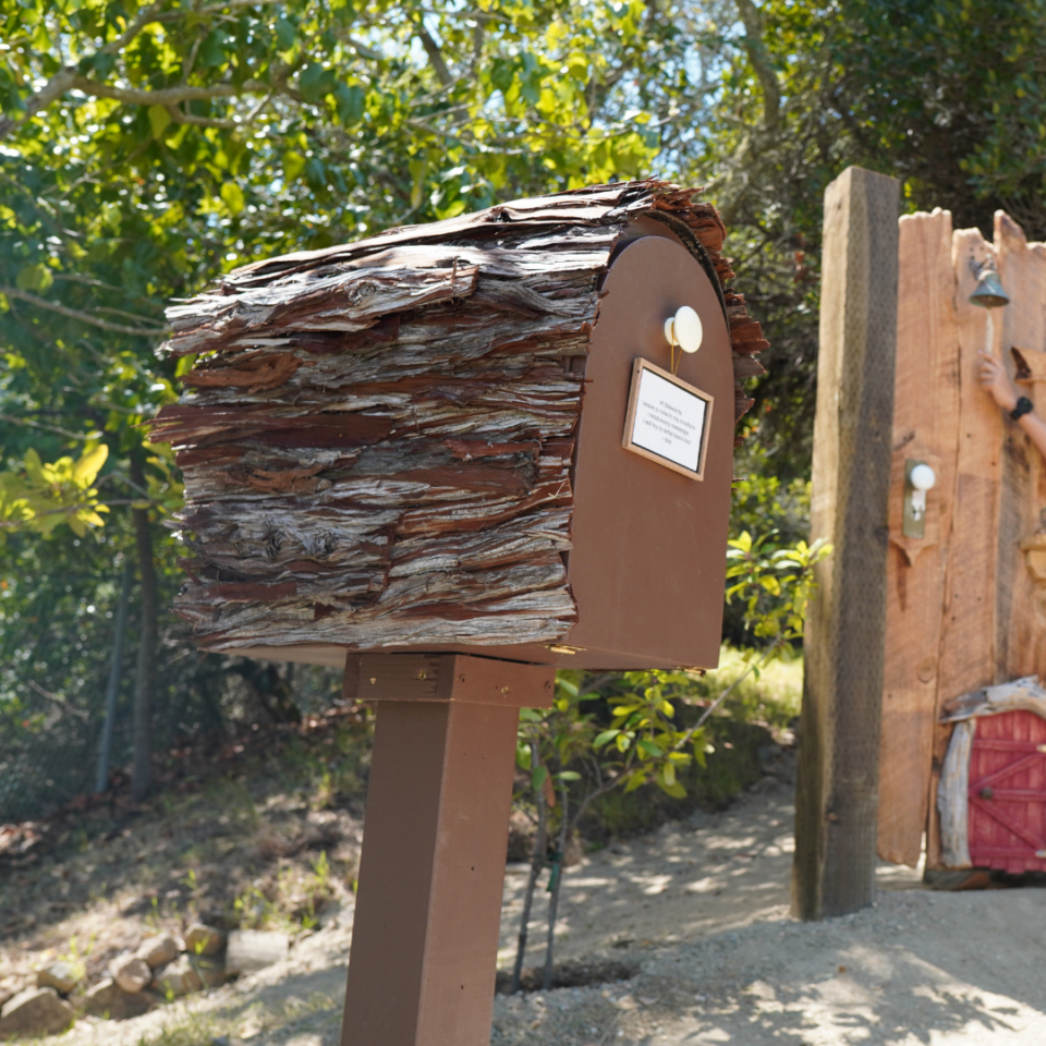 Log-shaped mailbox with bark-like shingles on a post in a sunny yard.