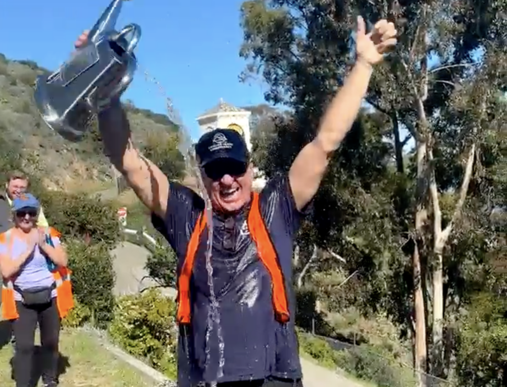 Conservancy volunteer raises a trophy above his head as water splashes down, while spectators applaud in the background on a sunny day on Catalina Island.