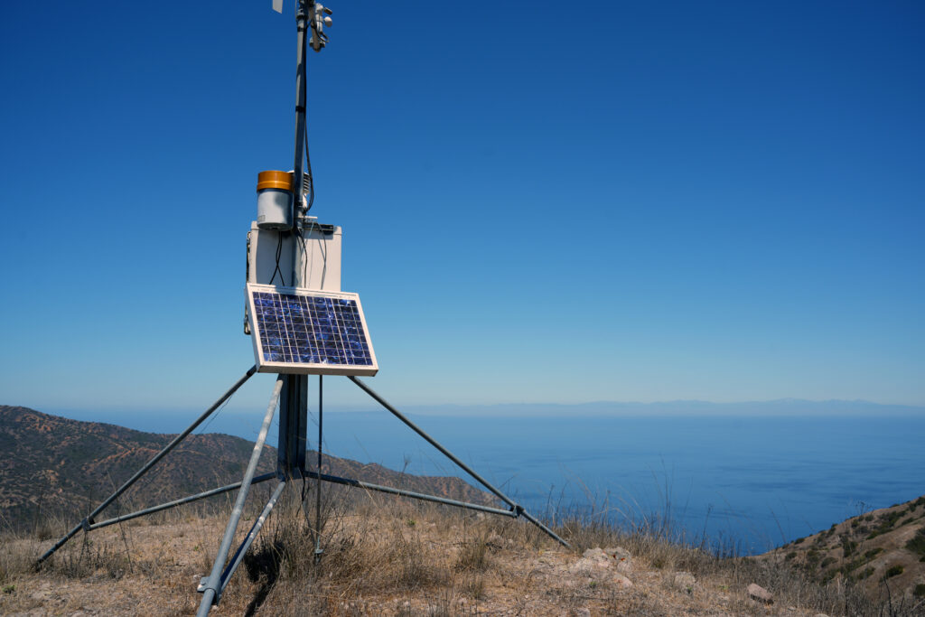 Solar panel mounted on a metal tripod in a dry hillside landscape under a clear blue sky