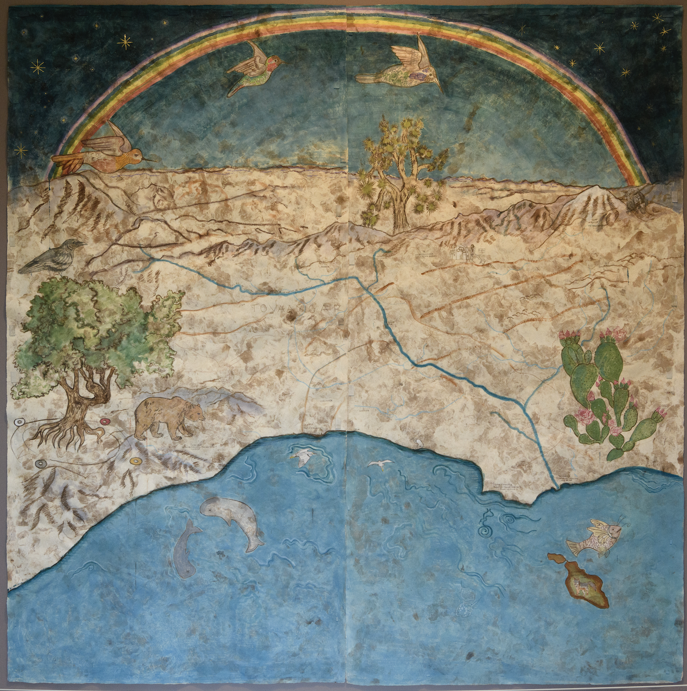 A panoramic desert map with a dark night sky, a bright rainbow arc, flying birds, a rocky horizon, a Joshua tree, a green tree, cacti with pink flowers, a bear and other wildlife, and a blue sea at the bottom containing dolphins and fish.